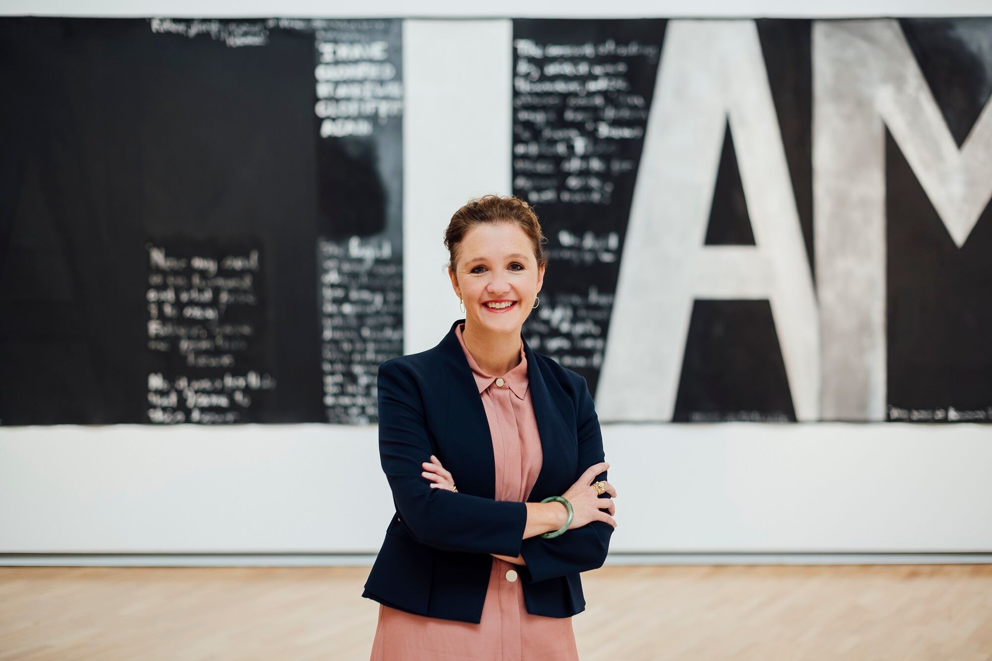 Image: New Auckland Art Gallery Director Kirsten Paisley
Image Credit:  Photography by Rohan Thomson. Artwork shown in background: Colin McCahon, Victory over death 2, 1970, National Gallery of Australia. Gift of the New Zealand Government 1978