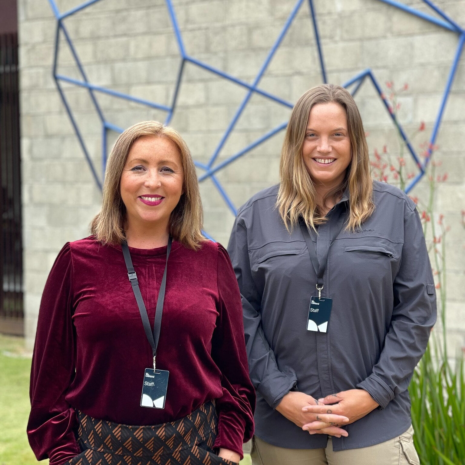 Two women in front of building and a blue geometric sculpture.