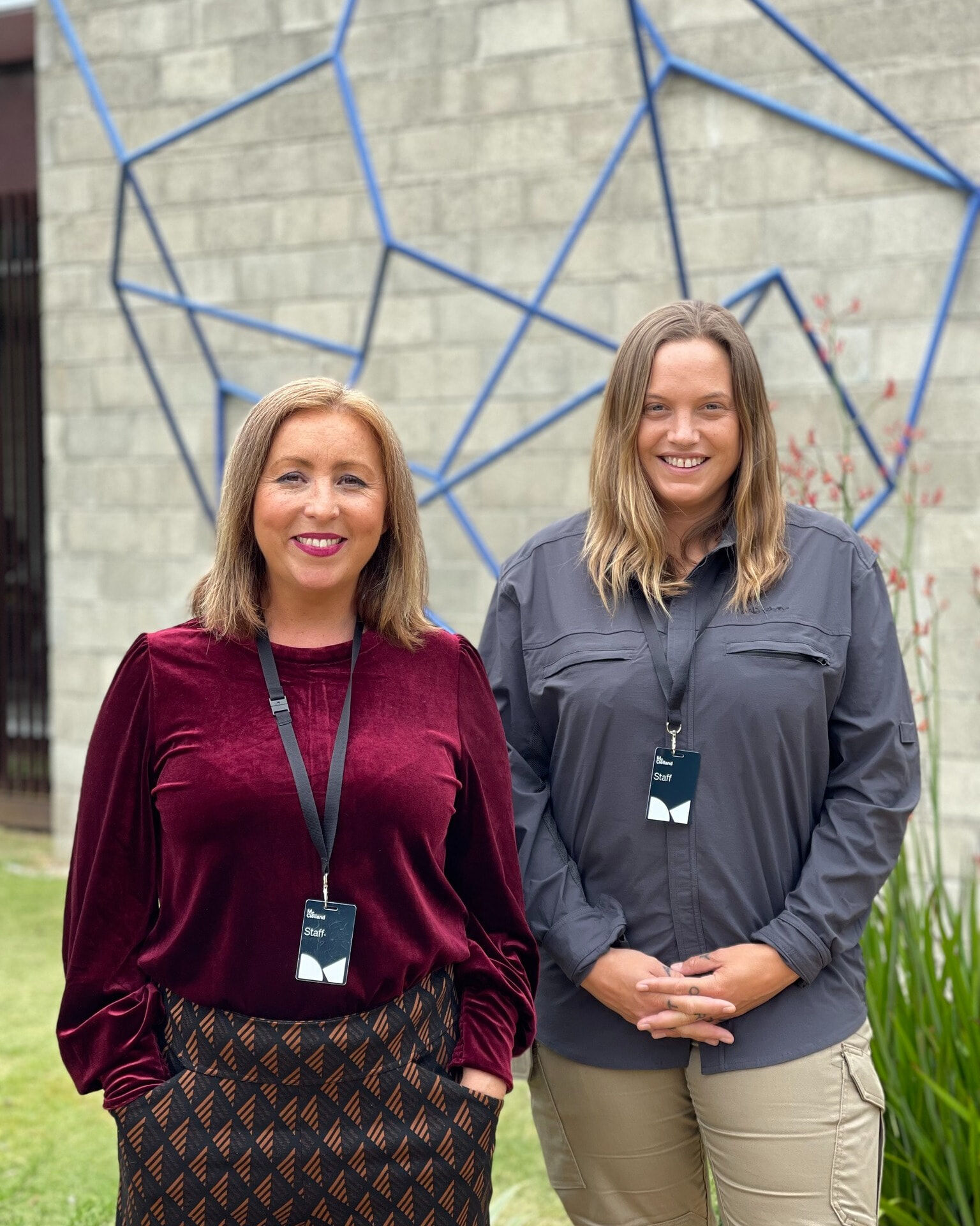 Two women in front of building and a blue geometric sculpture.